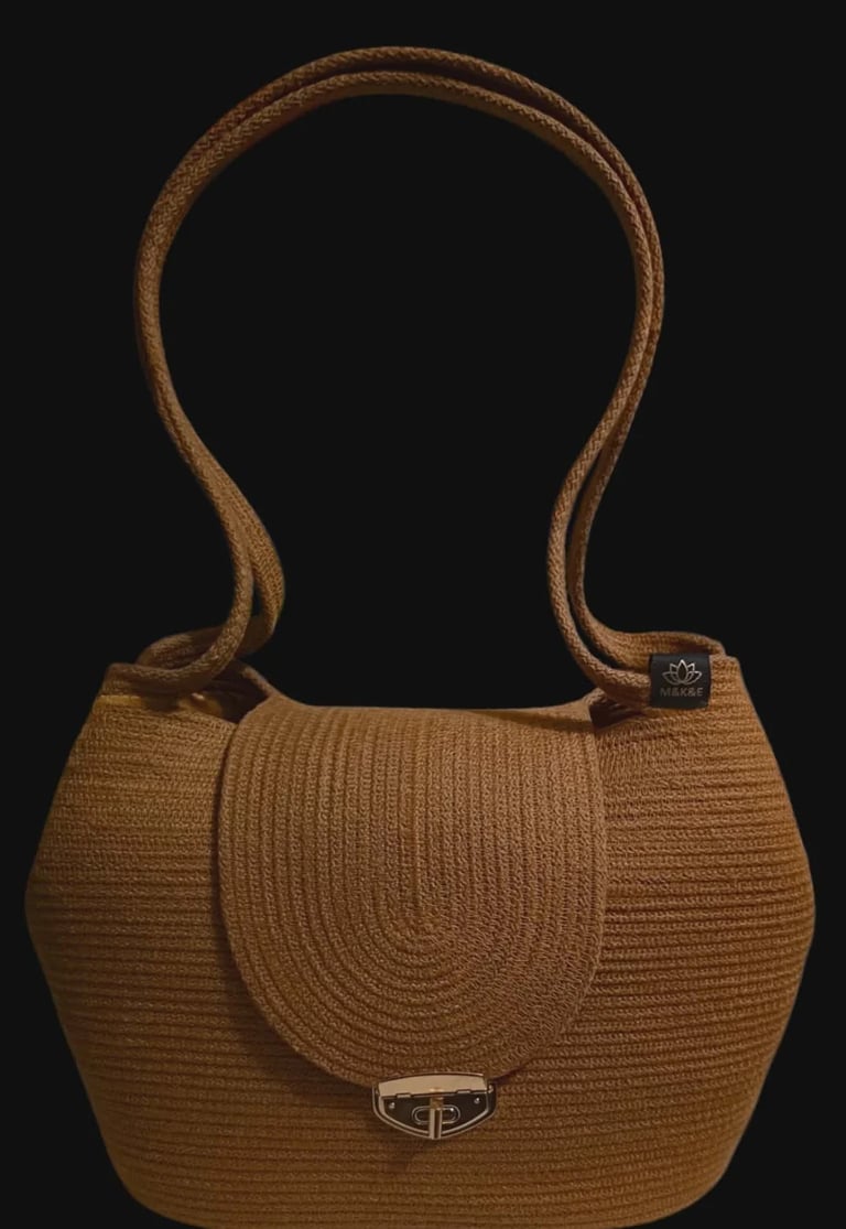 Brown woven straw handbag with rope handles and metal clasp on black background