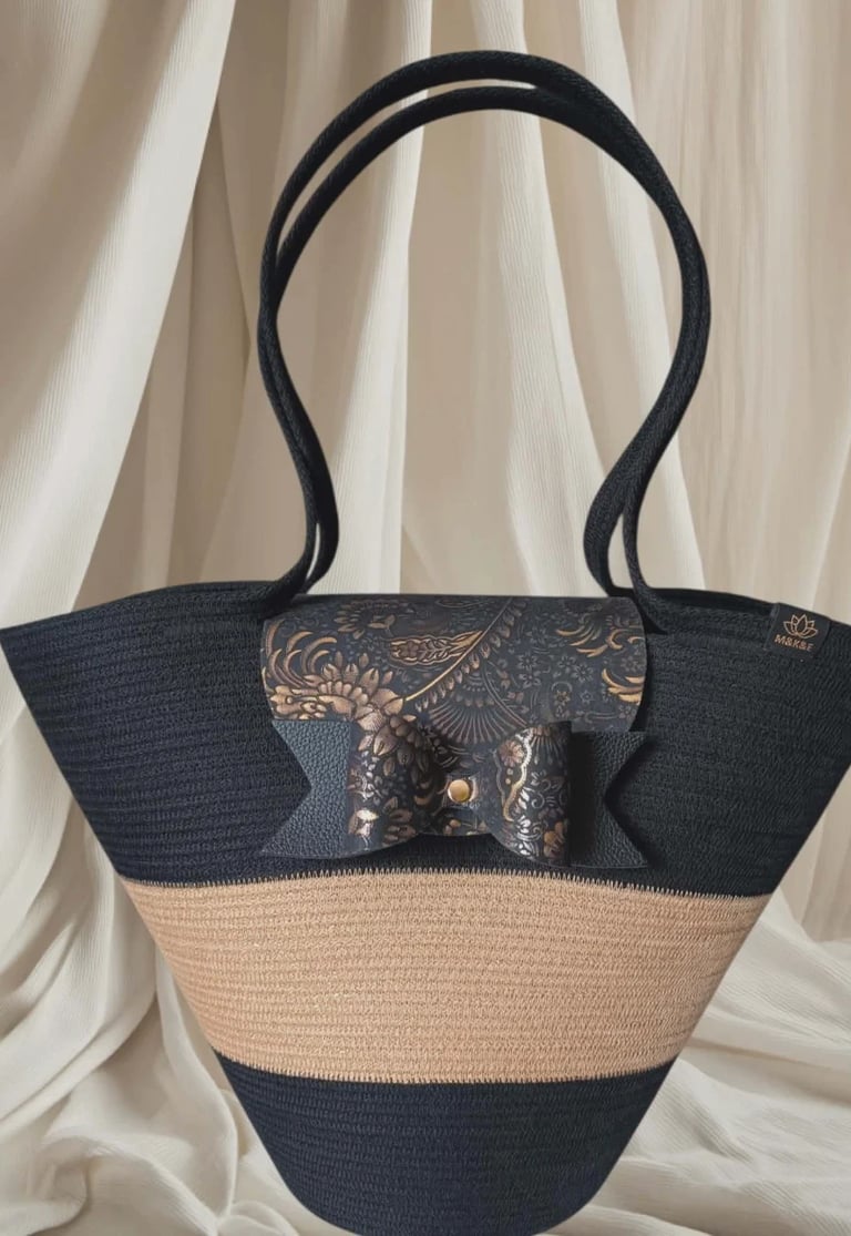 Black and beige striped woven tote bag with decorative metallic clasp displayed against cream drapes