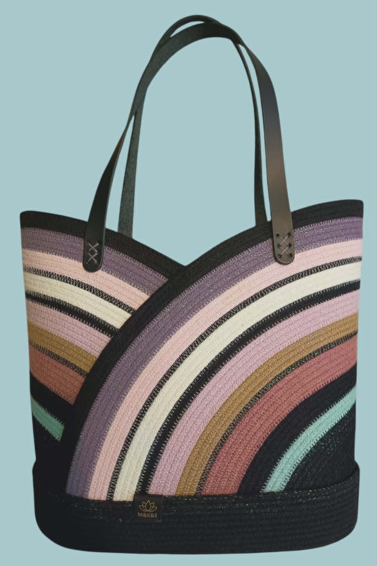 Tote bag with colorful rainbow striped pattern and black leather handles on light blue background