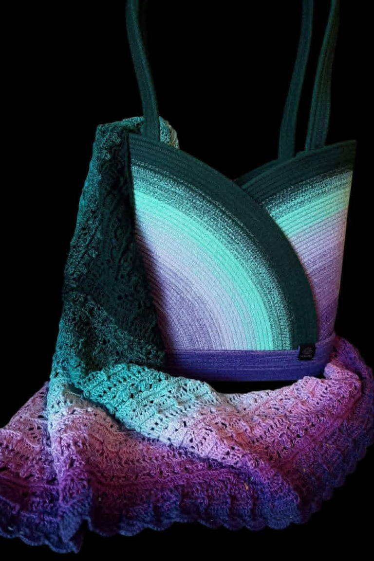 Colorful knit tote bag with gradient ombre effect transitioning from teal to pink and purple against a black background