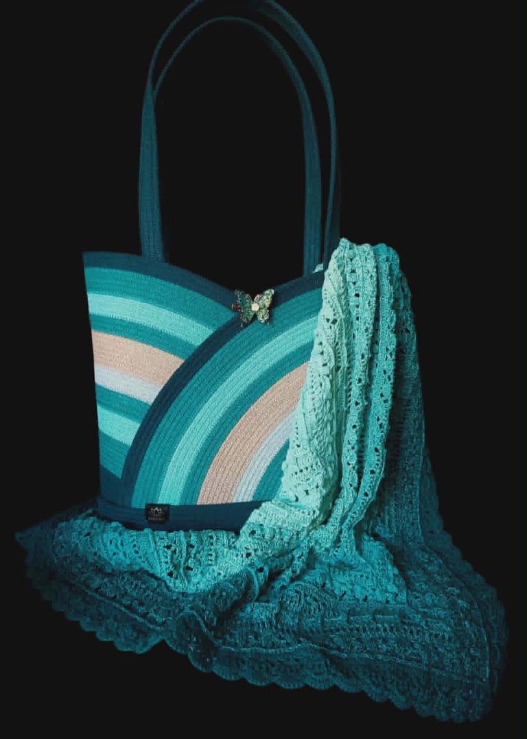 Turquoise striped tote bag with decorative lace shawl draped over it on black background