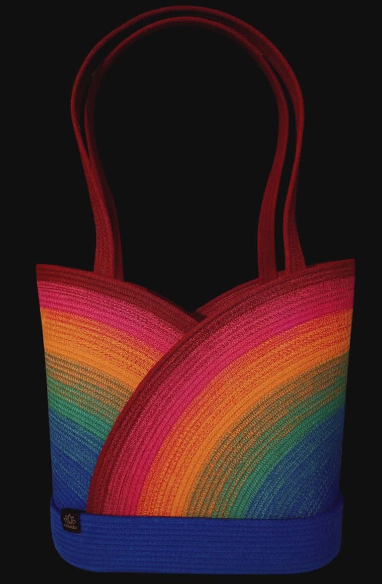 Rainbow striped tote bag with red handles against a black background