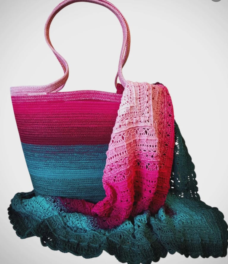 Colorful woven tote bag with pink, teal, and black horizontal stripes, draped with matching knit scarves or shawls