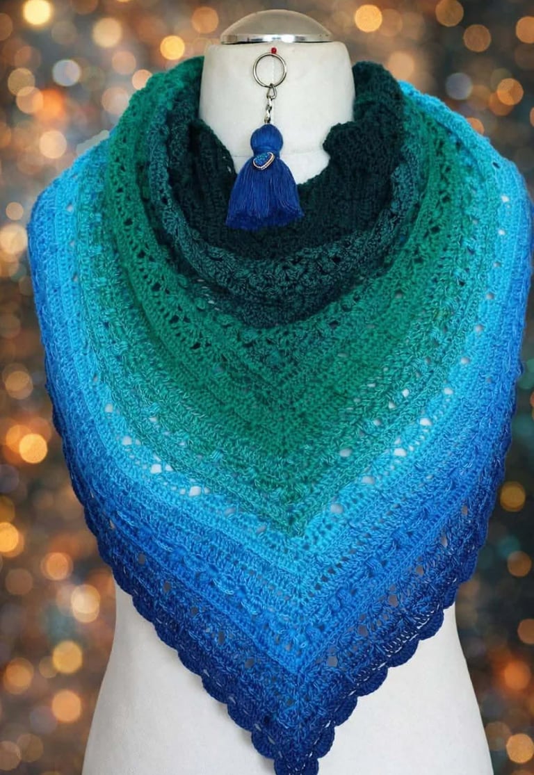 Ombre knitted shawl in gradient blue and teal tones displayed on a mannequin with blue tassel keychain and bokeh background