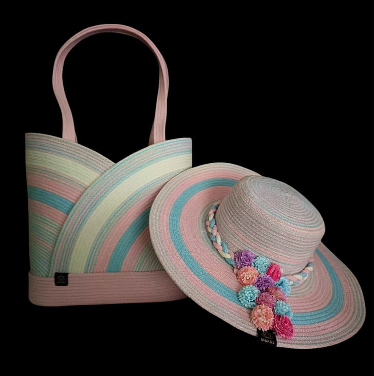 Pastel striped tote bag and wide-brimmed straw hat with colorful pom-pom trim on black background
